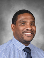 Desmond Chisholm is wearing a blue dress shirt and tie.